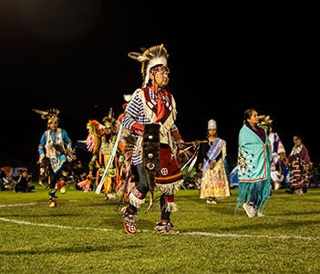 Dancers in traditional Native American clothing dancing on sports field at nighttime event